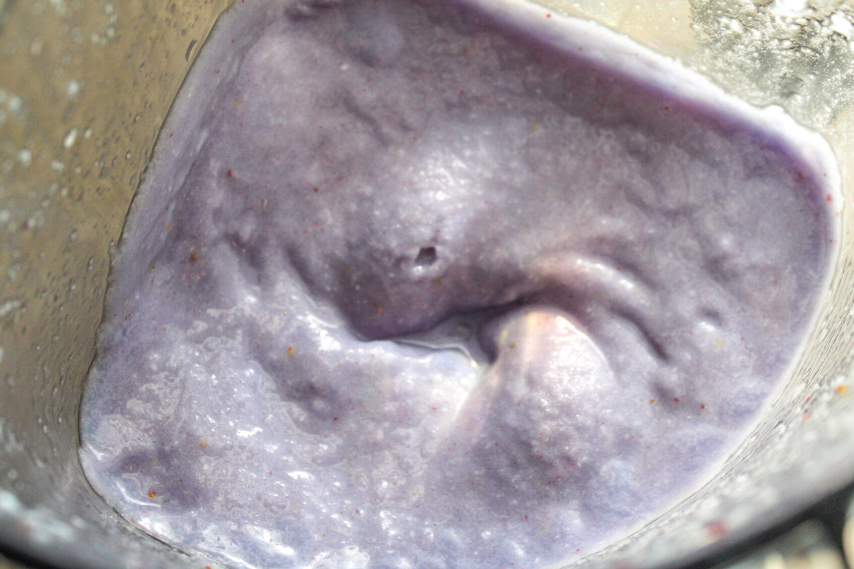Up close blender pitcher of a 5 minute strawberry coconut smoothie with blue spirulina making it lavender purple in color.