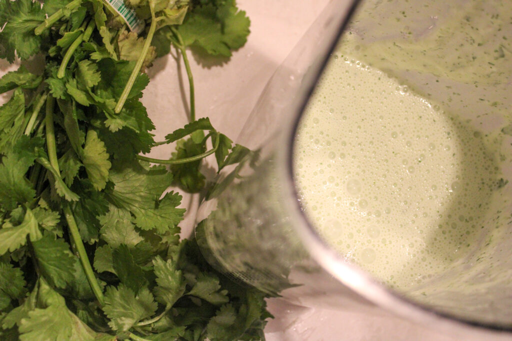 An arial view of Cilantro Scallion Crema in a blender with fresh cilantro sitting next to it.