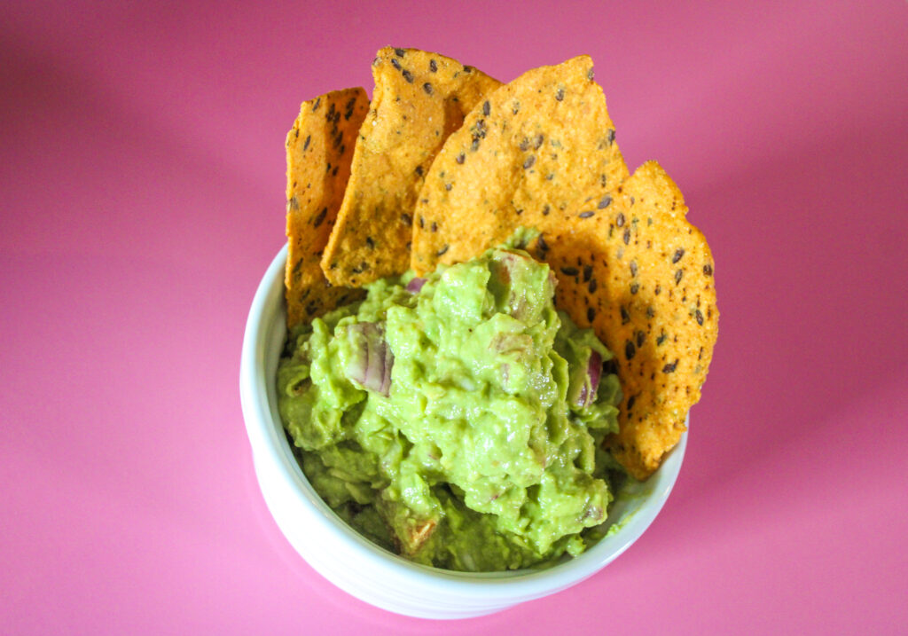 aerial view of orange chips in guac on a bright pink shadowy background
