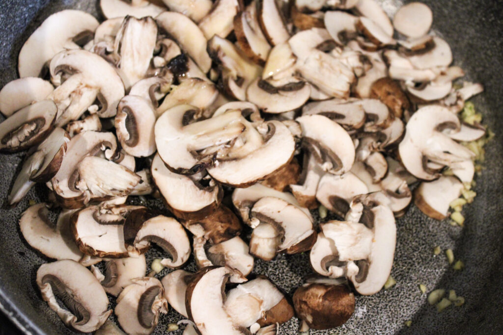 A large sauce pan with slices mushrooms and minced garlic.