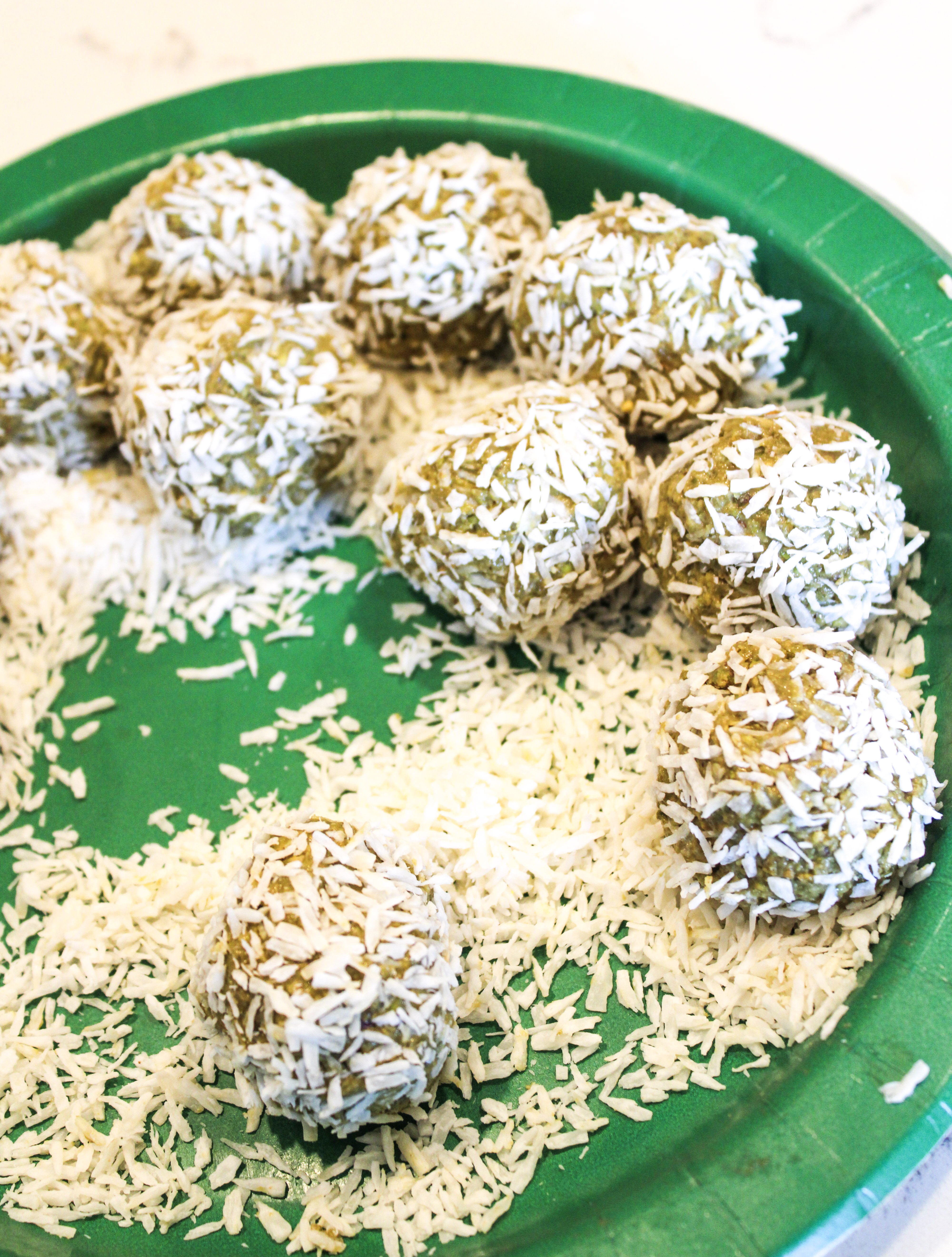 Pistachio bites covered in shredded cocobut on a green plate.
