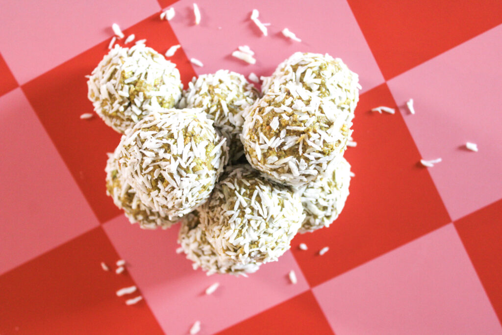 Pistachio bites coated in shredded coconut on a pink and red checkered background.