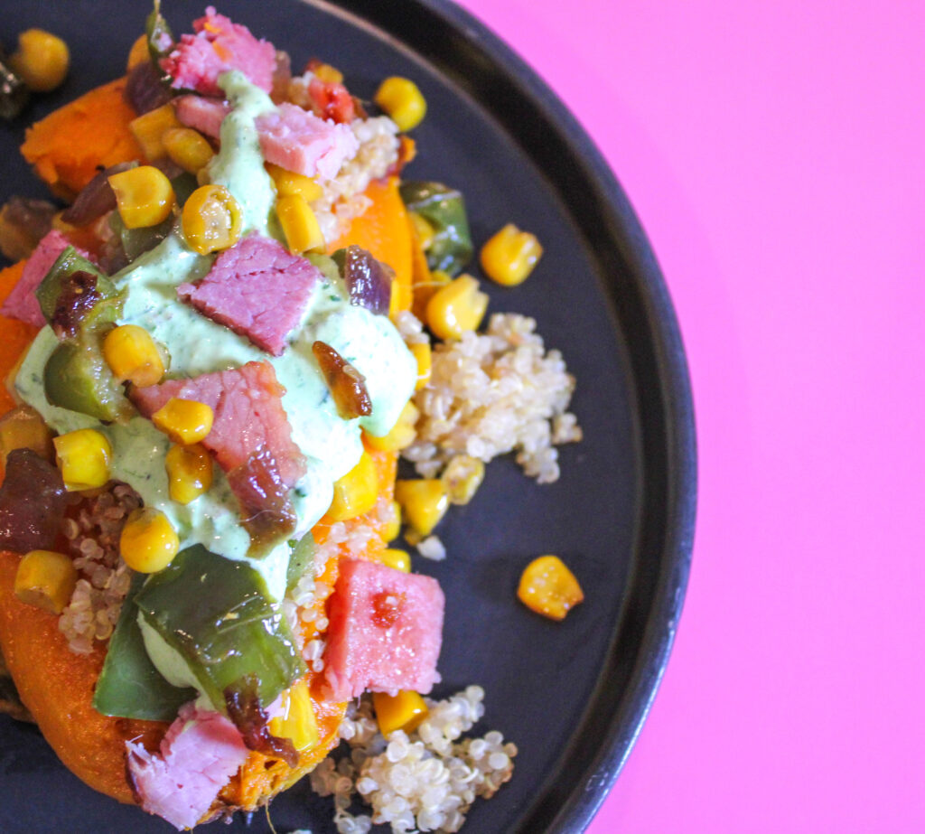 stuffed sweet potato with ham corn onions peppers and quinoa on a black plate with a pink background
