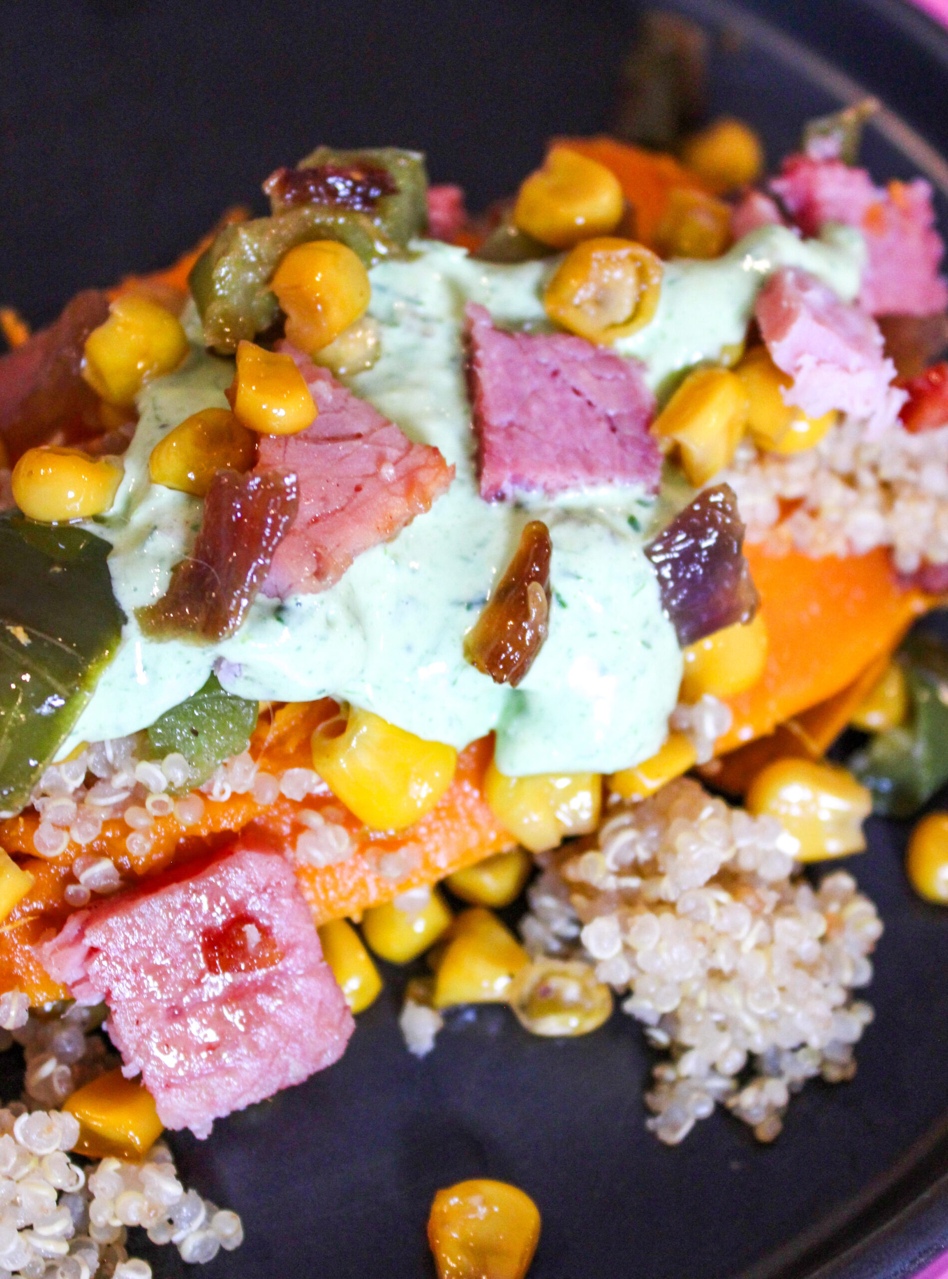 A stuffed sweet potato with ham corn onions peppers and quinoa on a black plate with a pink background