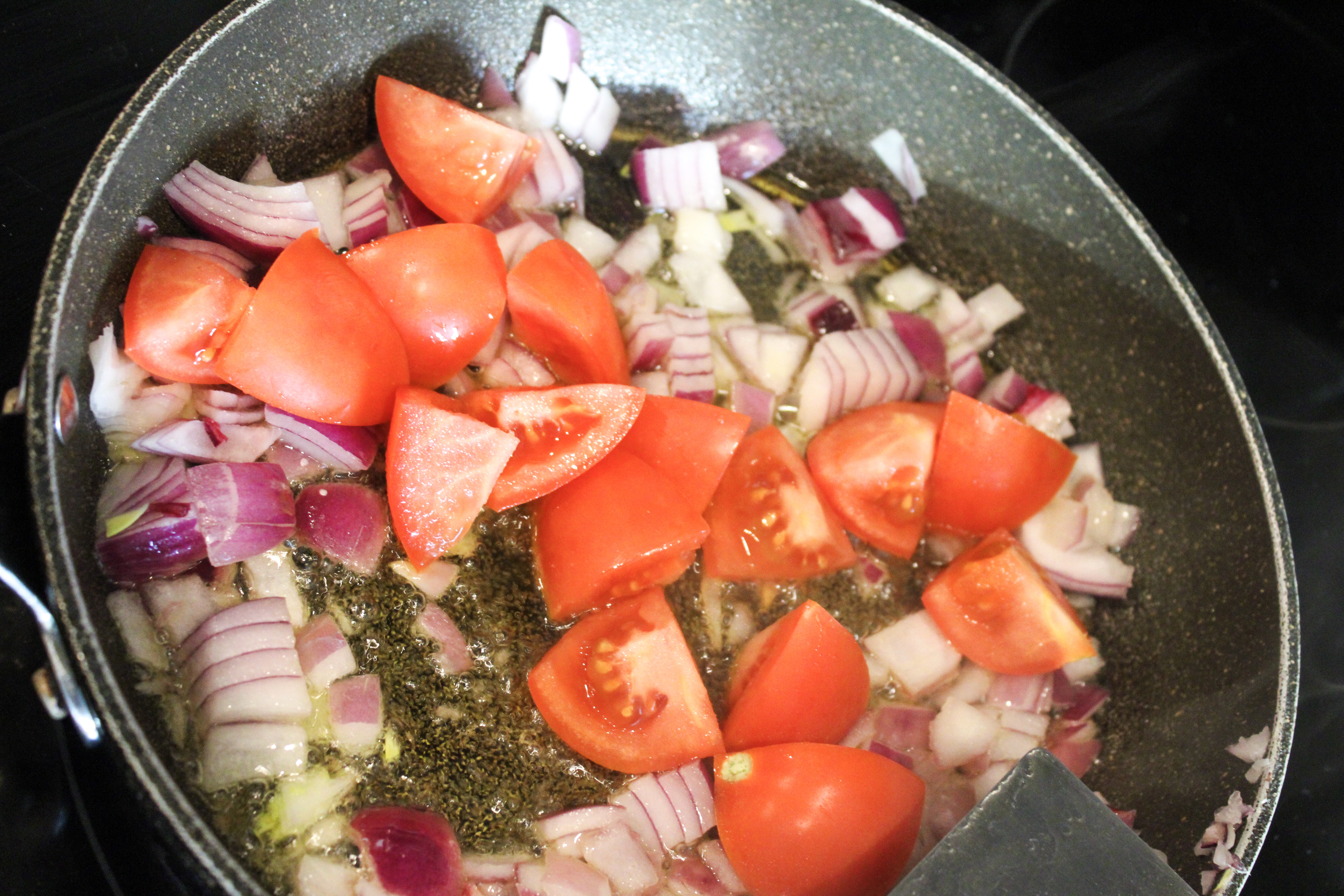 chopped tomatoes and diced onions cooking in a pan.