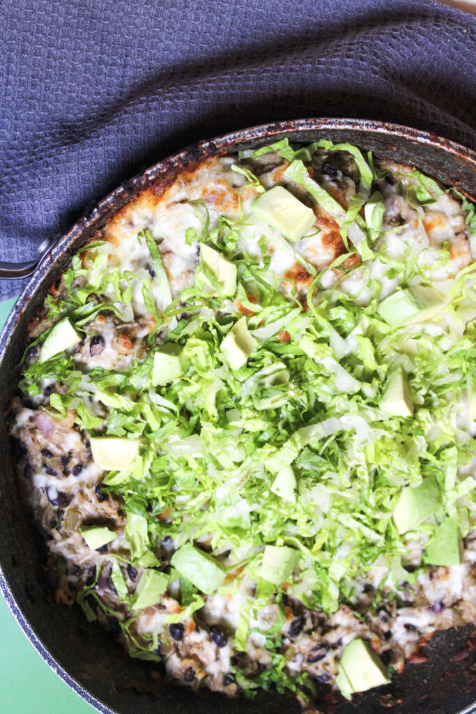 A completed enchilada skillet topped with shredded lettuce and diced avodacos.