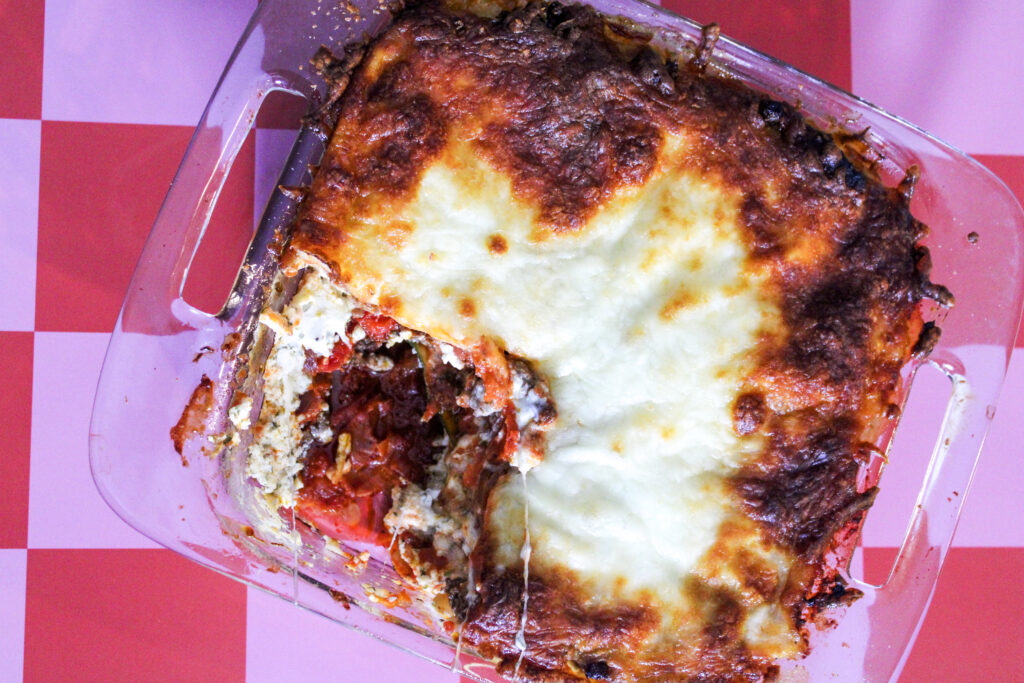Bakes Zucchini Lasagna with a piece cut out on a pink and red checkered background.