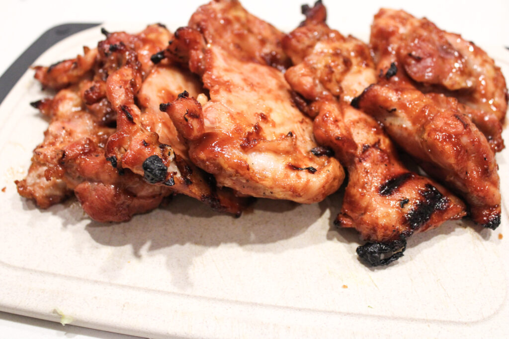 Grilled bbq chicken thighs on a cutting board.