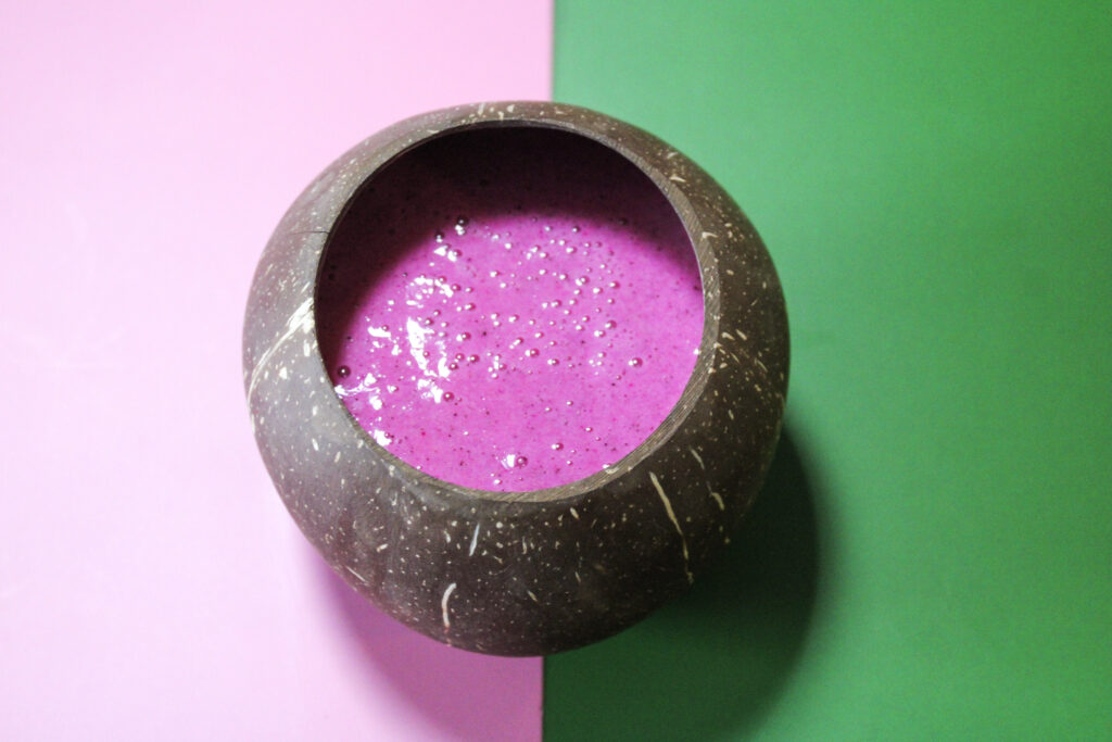 Pink coconut lemonade in a coconut on a pink and green background.